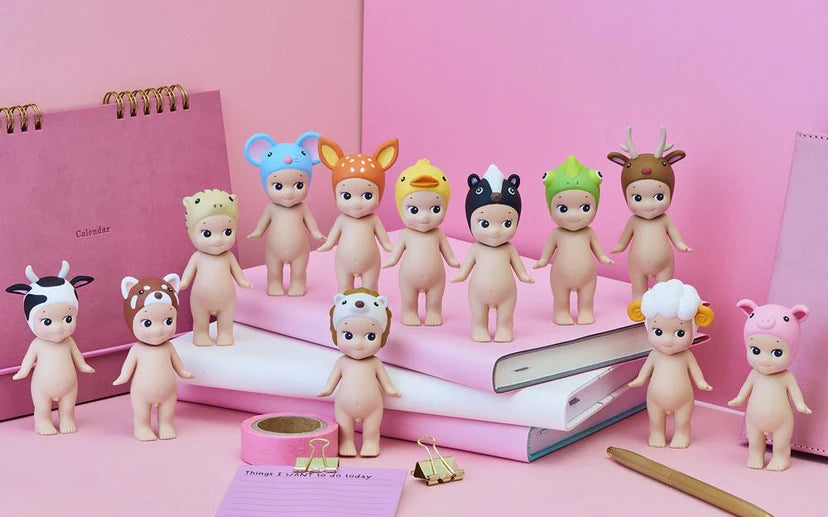 Set of small figurines with animal hats on a pink surface with stationery items.